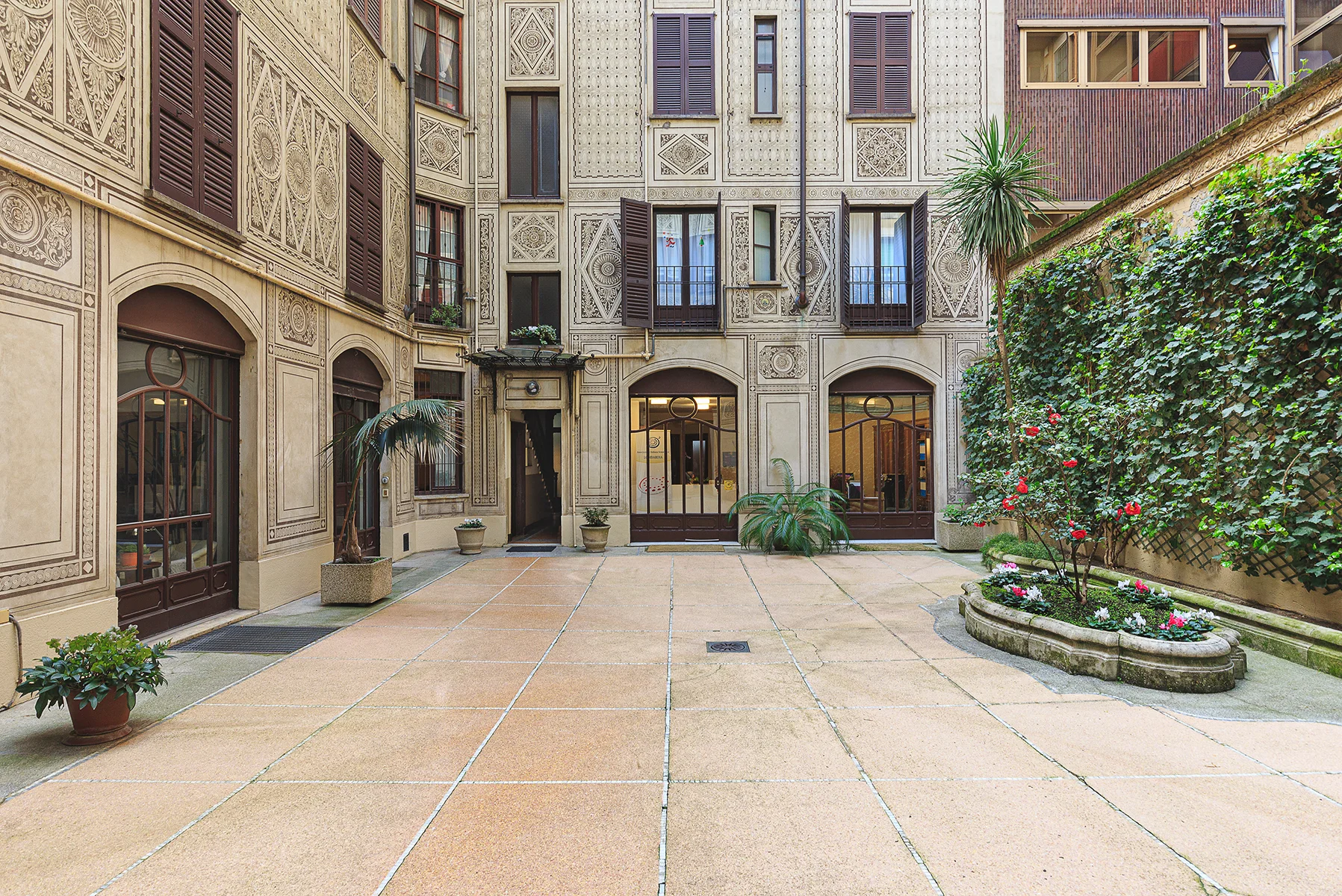 Cortile interno palazzo storico con facciata decorata, piante e portoni eleganti, Milano
